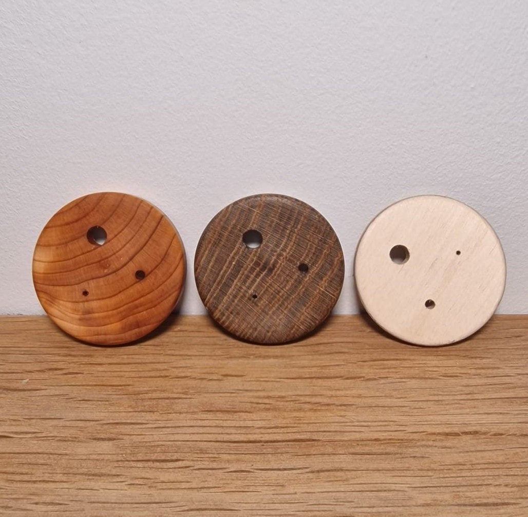An image with 3 Diz placed against a wall. From left to right they are made from Yew, Laburnum and Plywood. Each Diz has 3 holes drilled into them.